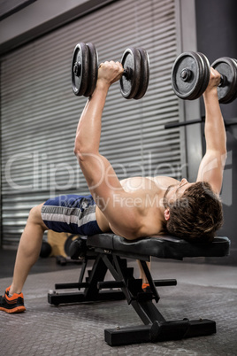 Shirtless man lifting heavy dumbbells on bench