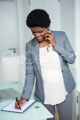 Pregnant businesswoman writing on notebook