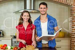 Portrait of woman cutting loaf of bread and man checking recipe