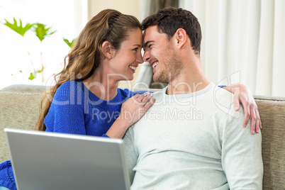 Young couple smiling face to face on sofa and using laptop