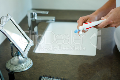 hands squeezing toothpaste onto a toothbrush