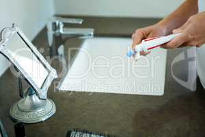 hands squeezing toothpaste onto a toothbrush