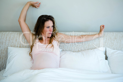 tired pregnant woman in bed stretching her arms