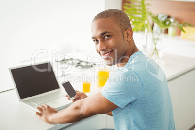 Smiling man using laptop and smartphone