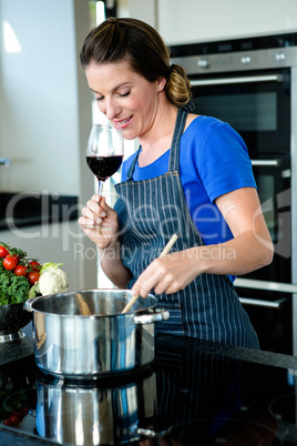 smiling woman cooking on the stove top and drinking red wine