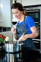 smiling woman cooking on the stove top and drinking red wine