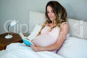 tired pregnant woman lying  in bed reading