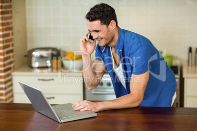 Young man using laptop and talking on phone