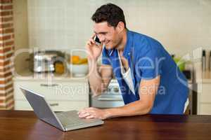 Young man using laptop and talking on phone