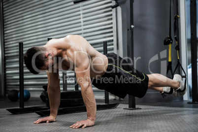 Shirtless man doing push up with the rope