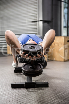 Muscular man on bench lifting dumbbell