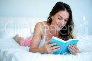 smiling woman lying in bed reading a book