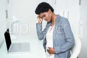 Pregnant businesswoman touching her head and belly