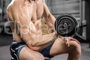 Shirtless man lifting heavy dumbbell on bench