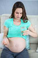 Pregnant woman holding glass of water and pills