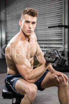 Shirtless man lifting heavy dumbbell on bench