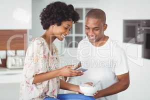 Happy couple eating breakfast and using smartphone