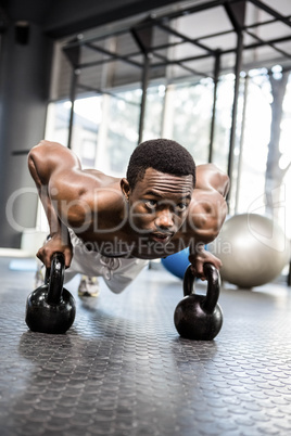 Muscular man doing push up with kettlebells