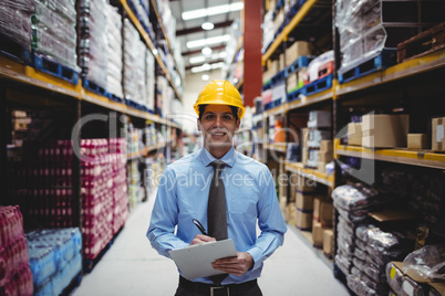 Smiling warehouse manager writing on clipboard