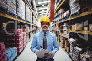 Smiling warehouse manager writing on clipboard