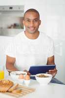 Young man using tablet and eating breakfast in kitchen