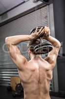 Rear view of shirtless man lifting heavy dumbbell