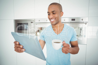 Smiling man using tablet and holding coffee