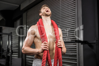 Shirtless man with battle rope around neck shouting