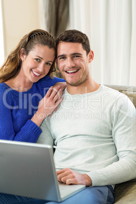 Young couple smiling face to face on sofa and using laptop