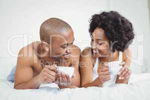 Happy couple lying on bed while holding cups