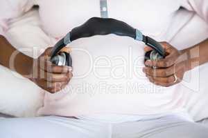 Pregnant woman holding headphone on belly