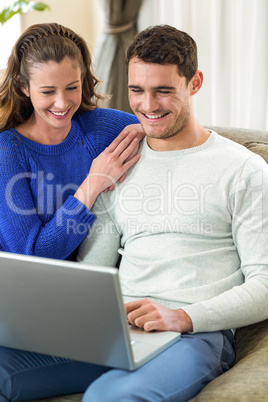 Young couple smiling face to face on sofa and using laptop