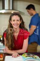 Woman checking the recipe book and man cooking on stove