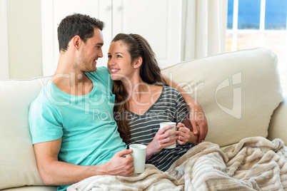 Young couple cuddling on sofa while having coffee