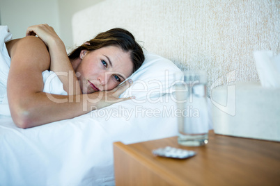 sick Woman lying in bed next to water and pills