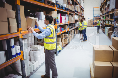 Smiling warehouse worker taking package in the shelf