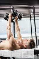 Shirtless man lifting heavy dumbbells on bench