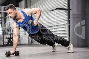 Muscular man doing push up with dumbbells