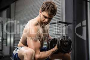 Shirtless man lifting heavy dumbbell on bench