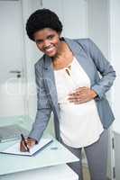 Pregnant businesswoman writing on notebook