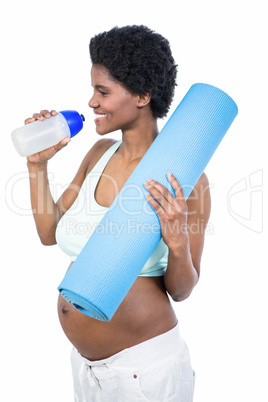 Pregnant woman holding water bottle and mat