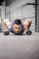 Muscular man doing push up with dumbbells