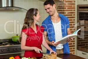 Woman cutting loaf of bread and man checking recipe book