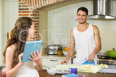 Man talking to woman while ironing a shirt