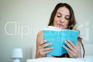 smiling woman reading a book in bed