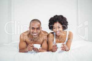 Happy couple lying on bed while holding cups