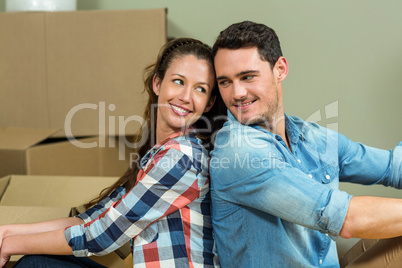 Young couple sitting back to back in their new house