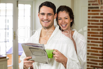 Portrait of young couple in bathrobe having tea and reading news