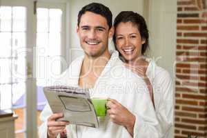 Portrait of young couple in bathrobe having tea and reading news