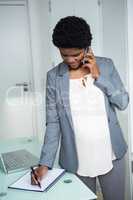 Pregnant businesswoman writing on notebook